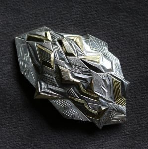 A textured silver brooch by artist and silversmith Miriam Hanid, Earth Brooch, 60x40mm, Britannia silver and lemon gilt, represented by Goldsmiths Fair